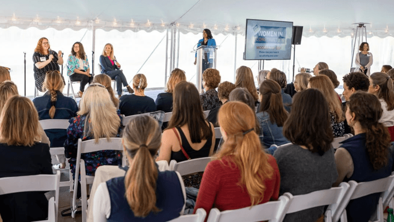 Audience at a women’s conference listening to speakers on stage under a tent